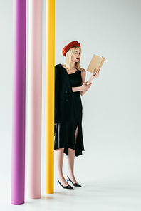 Stylish pretty woman in black dress reading book by colorful columns