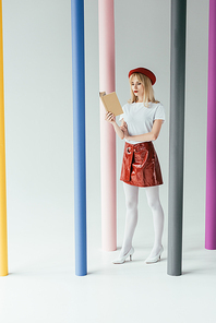 Attractive young woman reading book and posing by colorful pillars