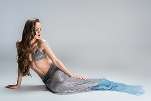 beautiful woman with mermaid tail lying on floor and looking away