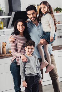 handsome latin father holding in arms cute daughter near wife and son at home