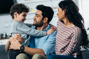 happy latin father hugging cute son near wife at home