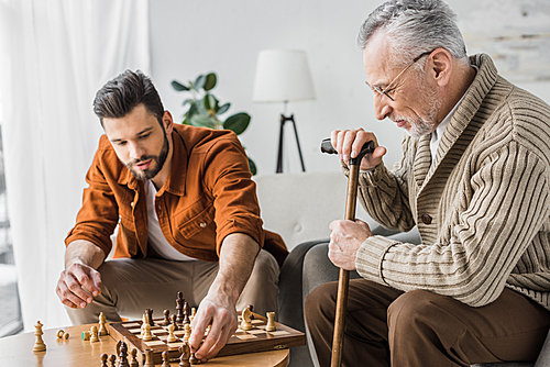 senior father in glasses playing chess with son at home