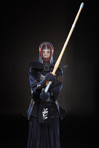 Kendo fighter in armor practicing with bamboo sword on black