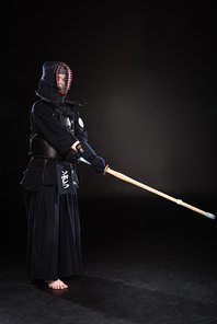 Full length view of kendo fighter in armor practicing with bamboo sword on black