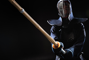 Kendo fighter in helmet holding bamboo sword on black