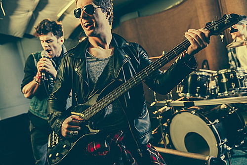 selective focus of cheerful guitarist in sunglasses playing electric guitar near rock band