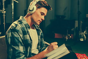 serious young composer listening music in headphones while writing in notebook