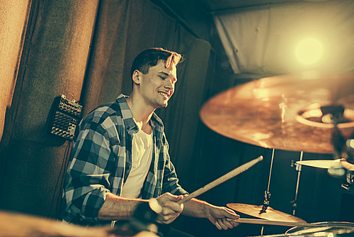 selective focus of handsome drummer holding drum sticks and playing drums