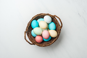 top view of colorful pastel easter eggs in wicker basket on white