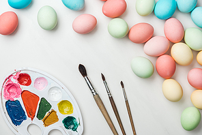 top view of pastel easter eggs with color palette and paintbrushes isolated on white