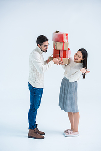 side view of cheerful multicultural couple looking at each other while holding stack of wrapped christmas gifts isolated on grey