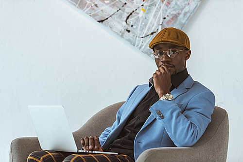 pensive african american businessman using laptop in modern office