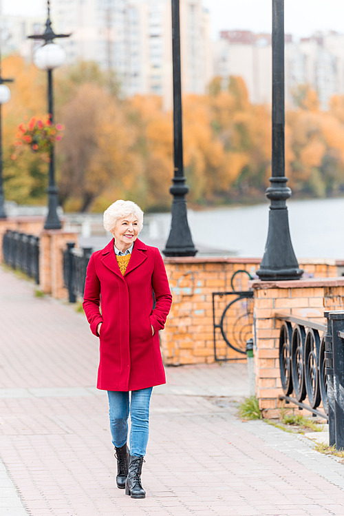 senior smiling woman in red coat walking on quay