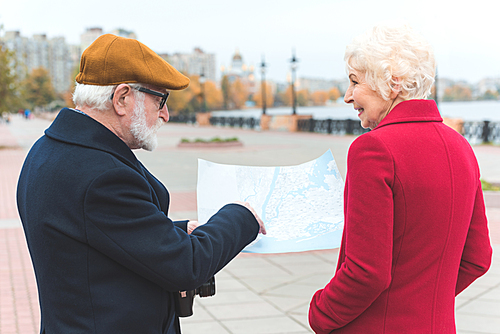 senior tourist couple looking at map while walking in city