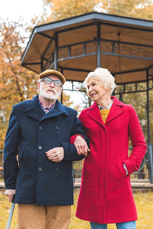 smiling senior couple walking in autumn park with gazebo on background