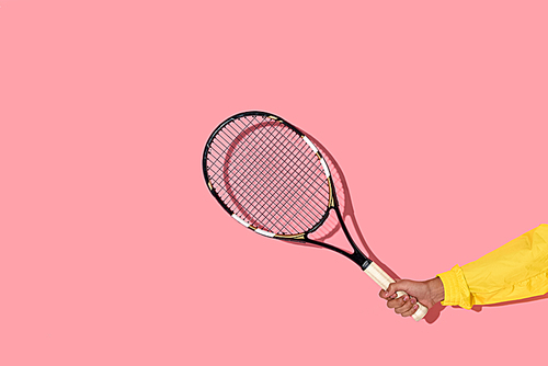 Close-up view of male hand holding tennis racket on pink background