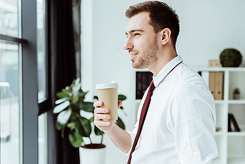 businessman holding disposable cup of coffee and looking at window