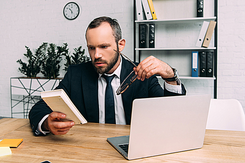 focused businessman with calculator and eyeglasses at workplace with laptop in office