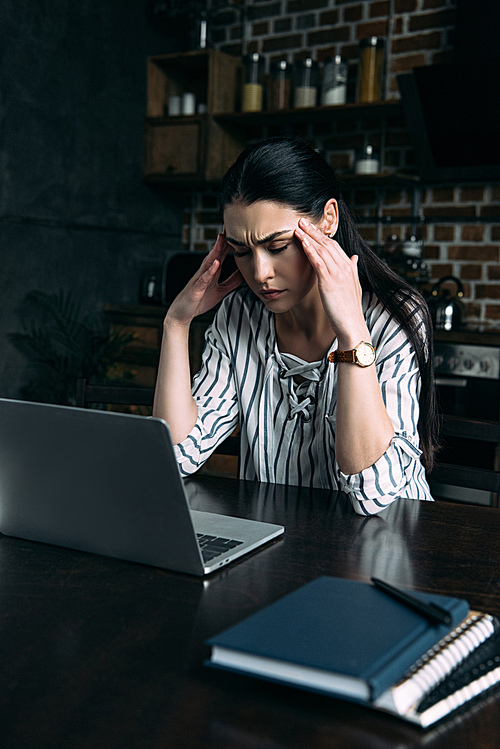stressed young woman with headache sitting on kitchen with laptop