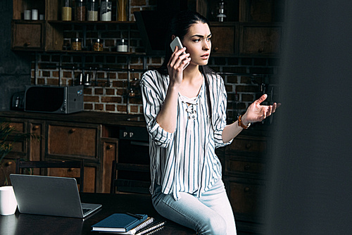 angry young woman talking by phone at kitchen