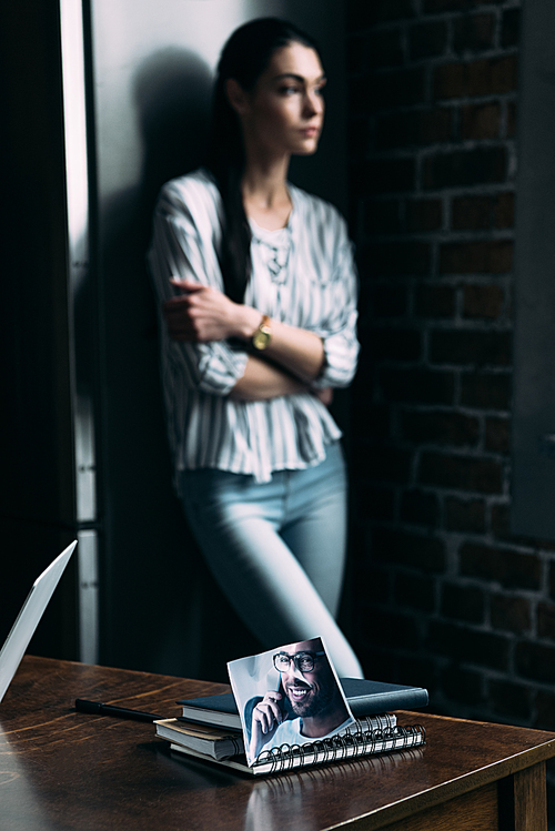 depressed young woman standing alone and looking away with photo of ex-boyfriend on foreground