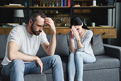 depressed young couple sitting on sofa at home after quarrel