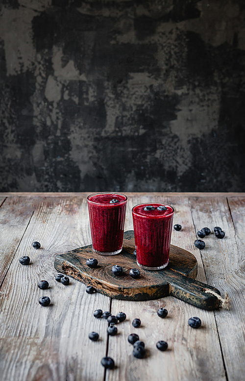 Delicious berry smoothie in glasses on rustic wooden board