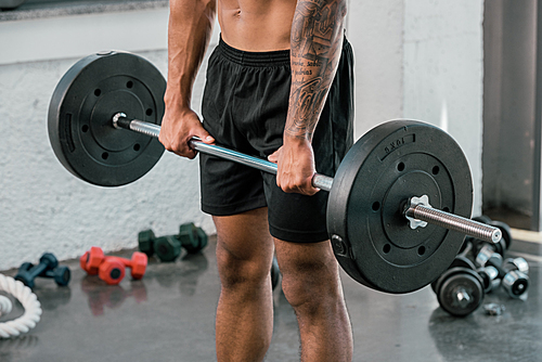 cropped shot of muscular young sportsman holding barbell in gym