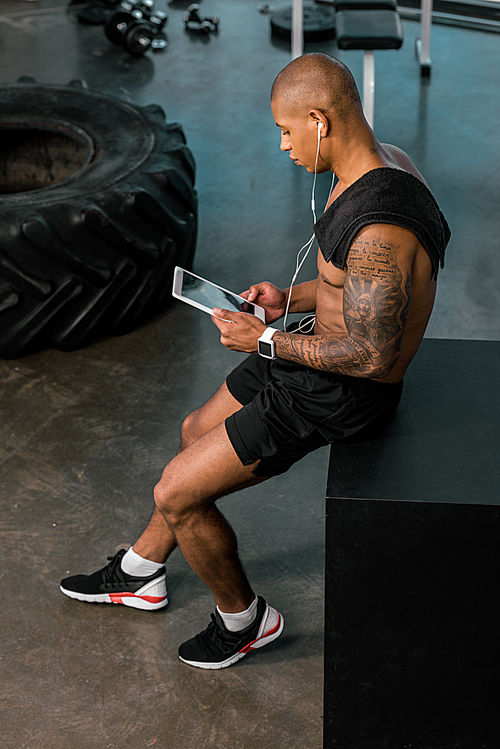 high angle view of young african american sportsman in earphones using digital tablet in gym