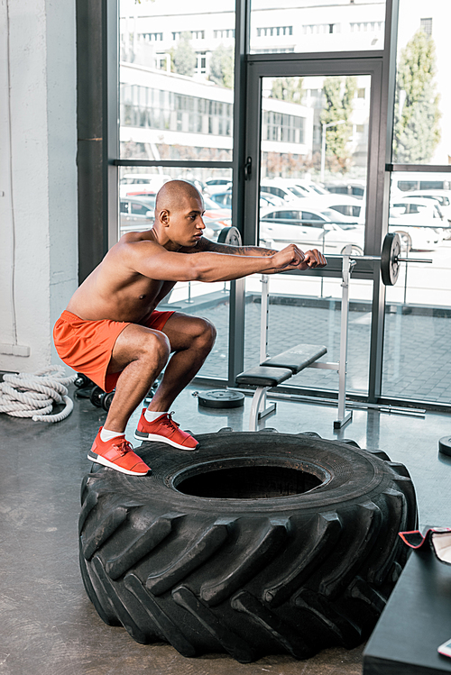 side view of shirtless african american athlete doing exercise on tire at gym