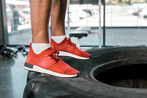 low section of sportsman in red sneakers standing on tire at gym