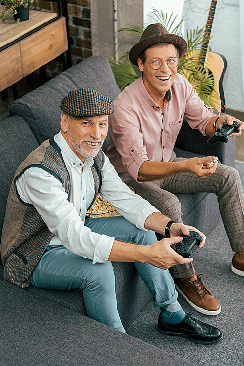 happy mature men playing with joysticks and smiling at camera, high angle view