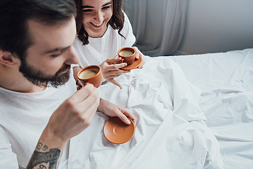 beautiful young couple drinking coffee while lying in bed in morning