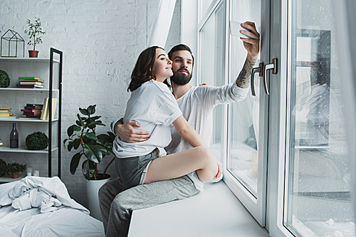 beautiful young couple taking selfie on smartphone at home