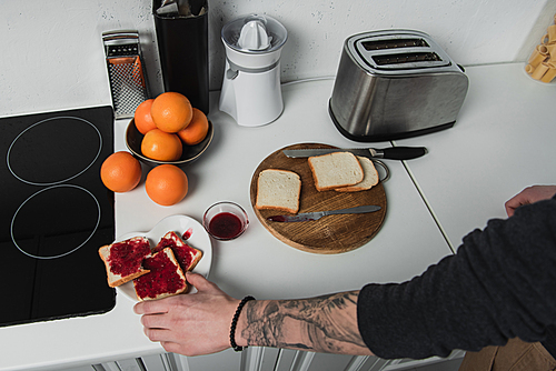 cropped view of man preparing toasts with jam during breakfast in kitchen