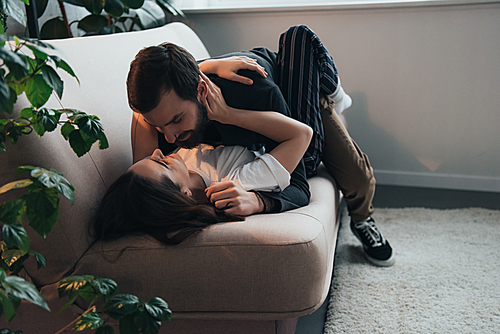 young passionate couple embracing while lying on couch at home