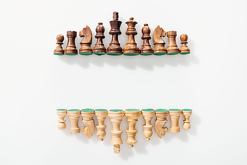 top view of rows made of brown and beige wooden chess figures on white background with copy space