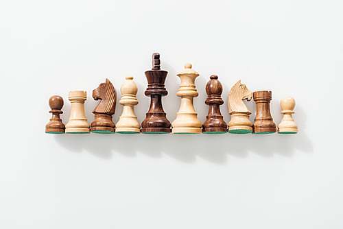 top view of row made of brown and beige wooden chess figures on white background
