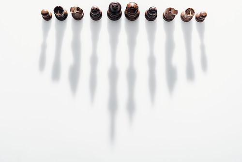 top view of brown chess figures with long shadows on white background