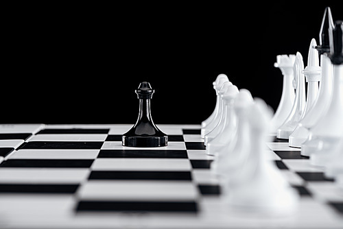 selective focus of chessboard with white chess pieces and black pawn in front isolated on black