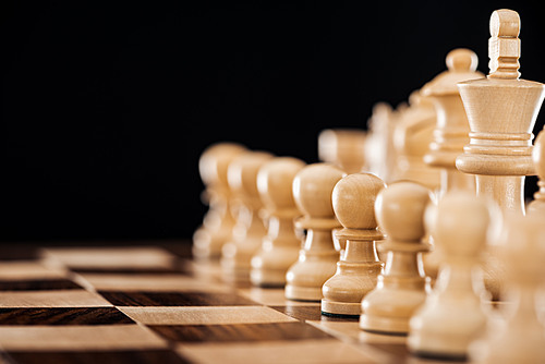 selective focus of wooden chessboard with beige chess figures isolated on black