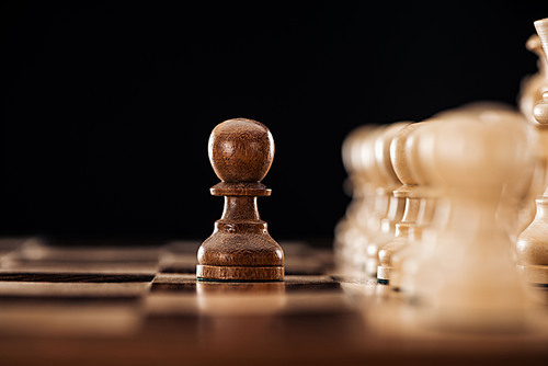 selective focus of wooden chessboard with chess pieces and pawn in front isolated on black