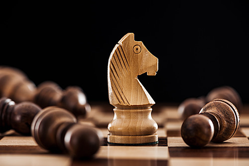 close up of chessboard with scattered wooden figures and knight isolated on black