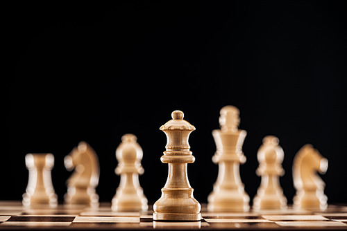 selective focus of beige wooden queen on chessboard isolated on black