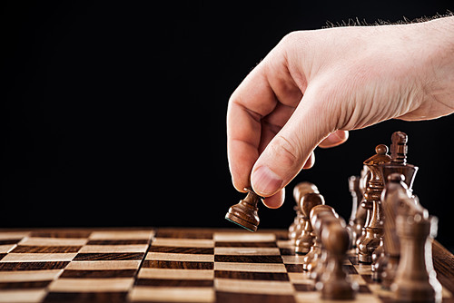 partial view of man doing move on wooden chessboard isolated on black