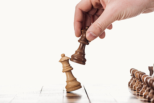 partial view of man holding brown queen near beige queen on wooden chessboard isolated on white