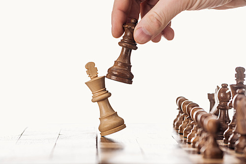 partial view of man holding queen near king on wooden chessboard isolated on white