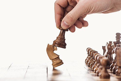 partial view of man holding pawn near knight on wooden chessboard isolated on white