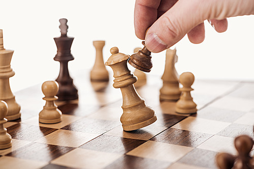 partial view of man doing move with brown pawn on wooden chessboard isolated on white