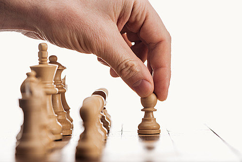 cropped view of man doing move with beige pawn on wooden chessboard isolated on white